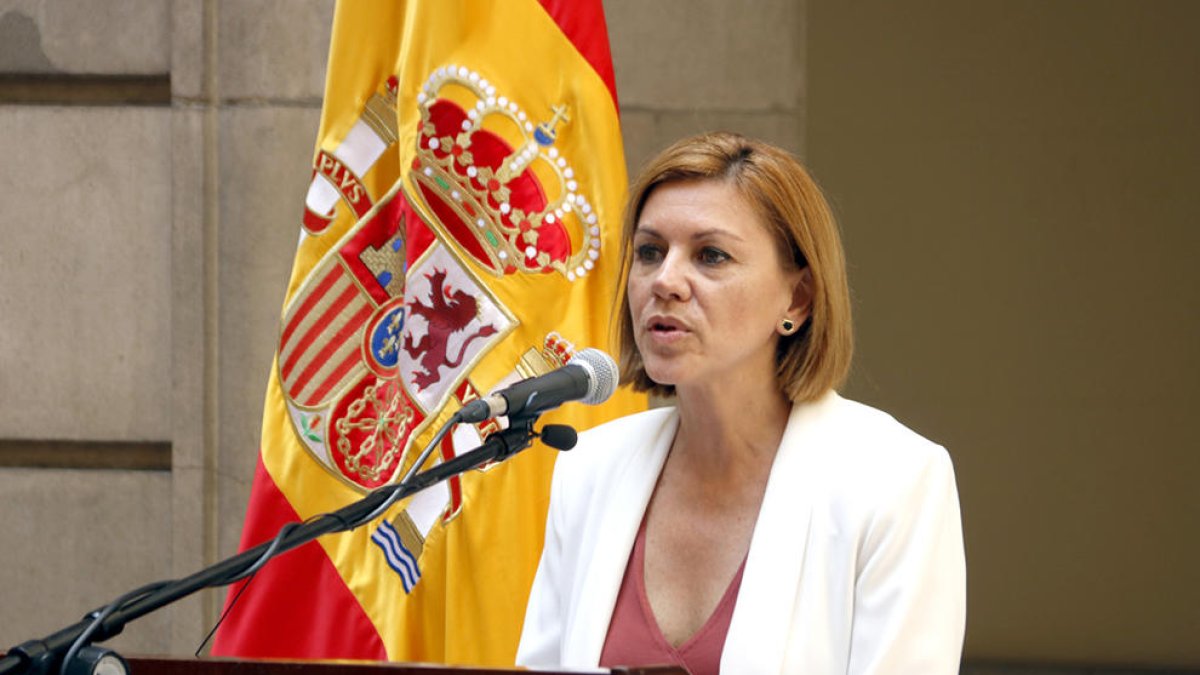La ministra de Defensa, María Dolores de Cospedal, hablando con una bandera española detrás.