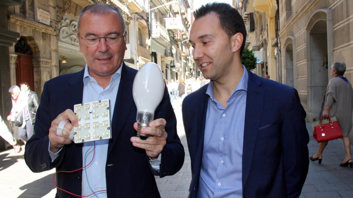 El alcalde de Reus, Carles Pellicer, y del concejal de Medio Ambiente, Daniel Rubio, mostrando la bombilla que se sustituirá por luz led, en la calle de Llovera de Reus, una de las calles que renovará alumbrado.