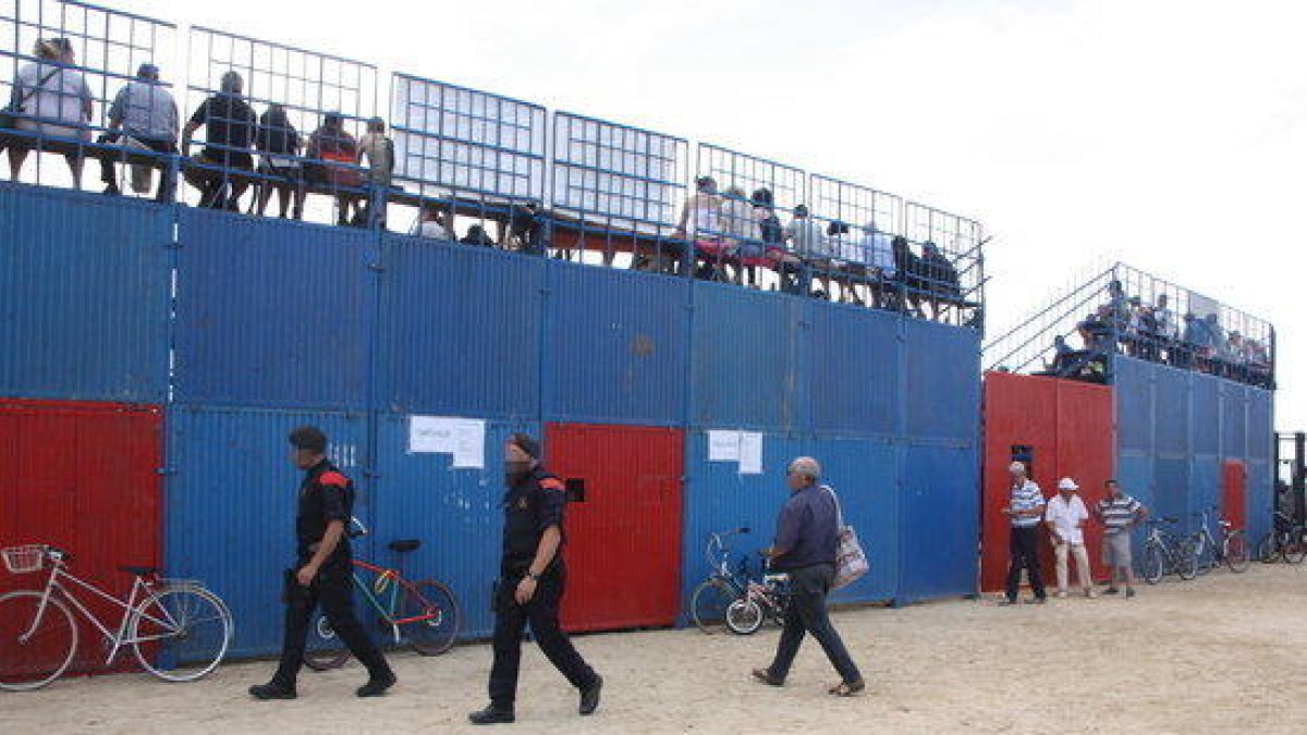 Dos Mossos d'Esquadra passen per davant de la plaça de bous de Sant Jaume d'Enveja.