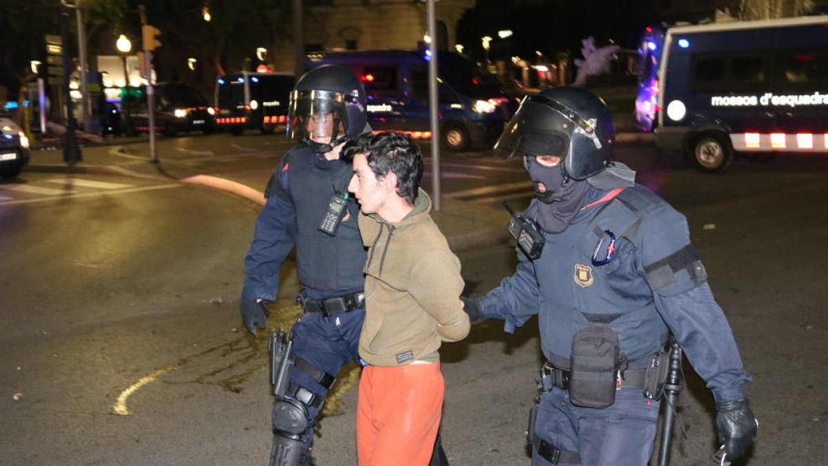 Plano medio de dos agentes y un manifestante detenido en la fuente del Centenari de Tarragona durante los disturbios en la ciudad.