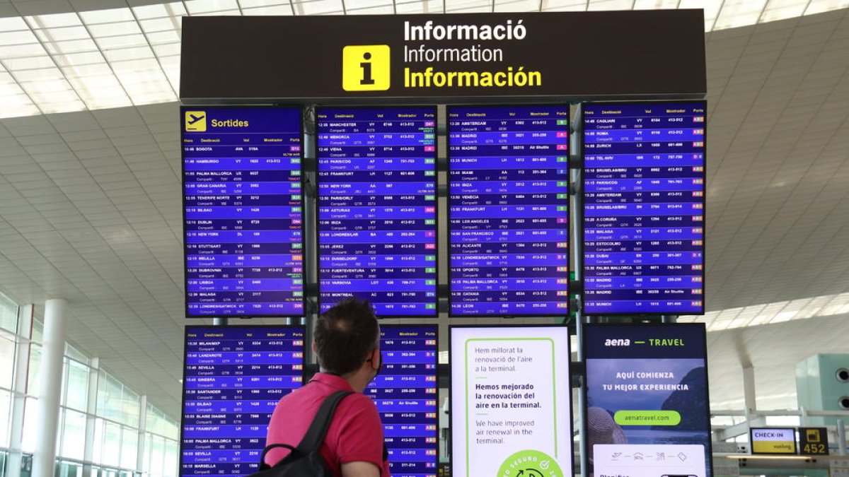 Un passatger mira els panells informatius de la terminal 1 de l'aeroport del Prat.