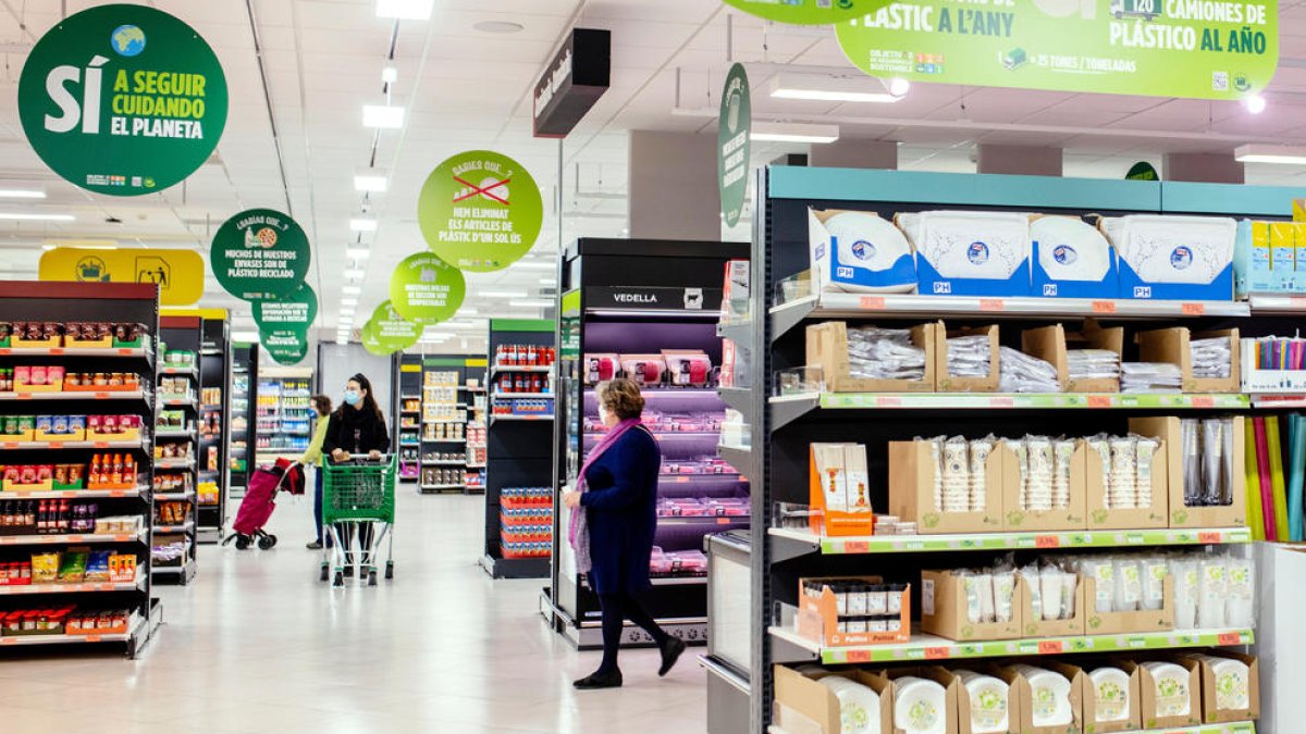 Pla general d'un supermercat de Mercadona amb clientes comprant i cartells sobre sostenibilitat el desembre del 2021. (Horitzontal)