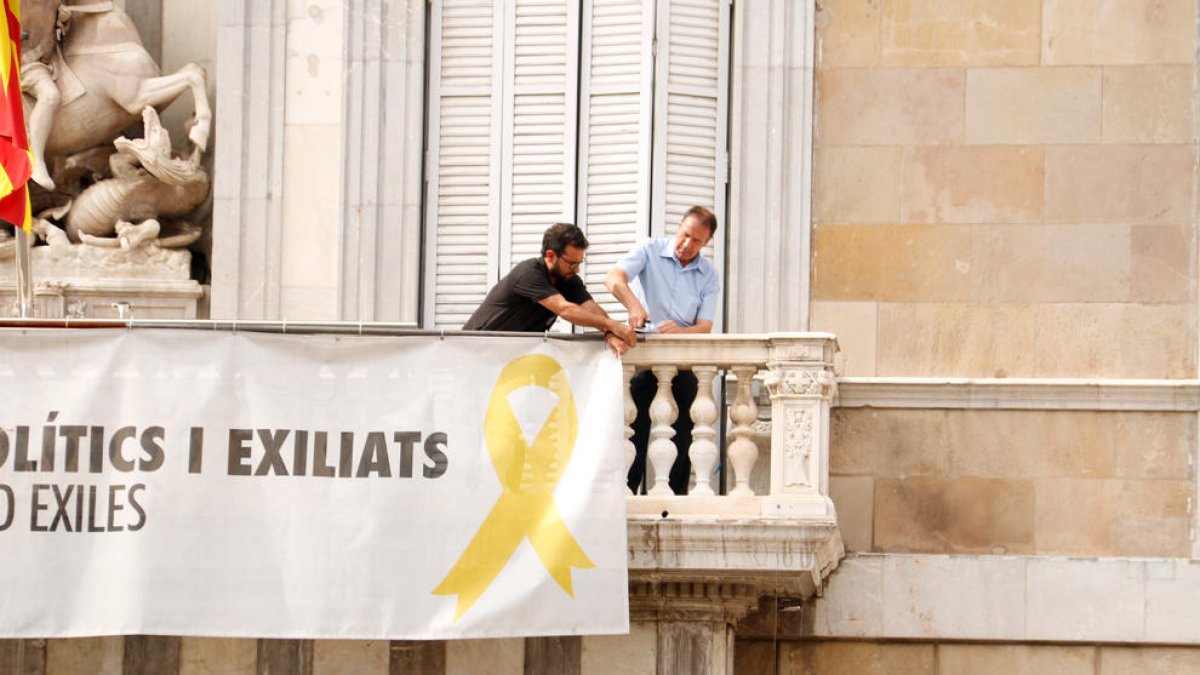 Dos treballadors comencen a treure la pancarta dels presos del Palau de la Generalitat.