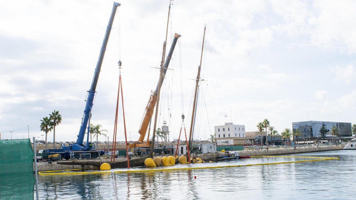 Dues grans grues comencen a treure de l'aigua l'Eleonora E enfonsat a la Marina Port Tarraco