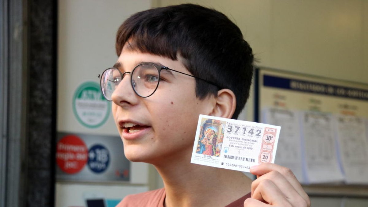 Un jove de 15 anys guanyador del primer premi del sorteig de Reis mostra una butlleta a l'administració de la Travessera de Gràcia.