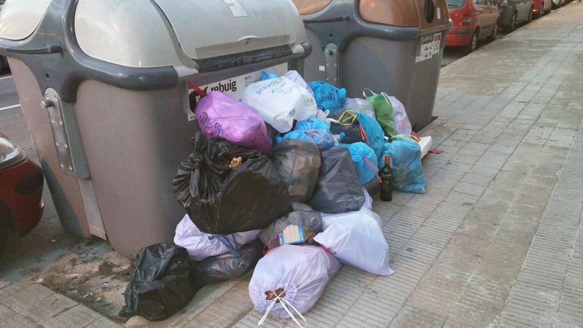 Un contenedor desbordado con la basura en la acera.