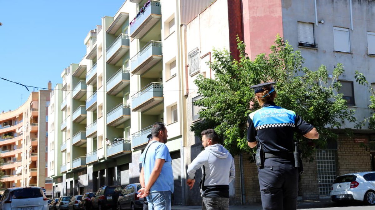 Agentes de la Guardia Urbana de Reus, en primer término, conversando con gitanos que han ocupado uno de los pisos, y encima de un balcón de las viviendas ocupadas, una mujer observándolos.