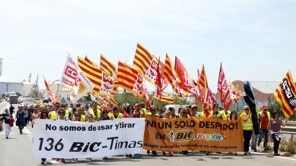 Plano general de los trabajadores de BIC Graphic en Tarragona, haciendo una marcha lenta encabezada por pancartas de protesta en la autovía de Salou, con el tráfico parado en el fondo. Imagen del 9 de mayo del 2017