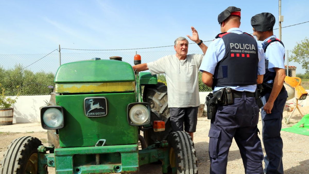 Plano general de dos agentes de los Mossos D'Esquadra conversando con un campesino al lado de su tractor en una masía de Vallmoll (Alt Camp), el 7 de julio del 2017