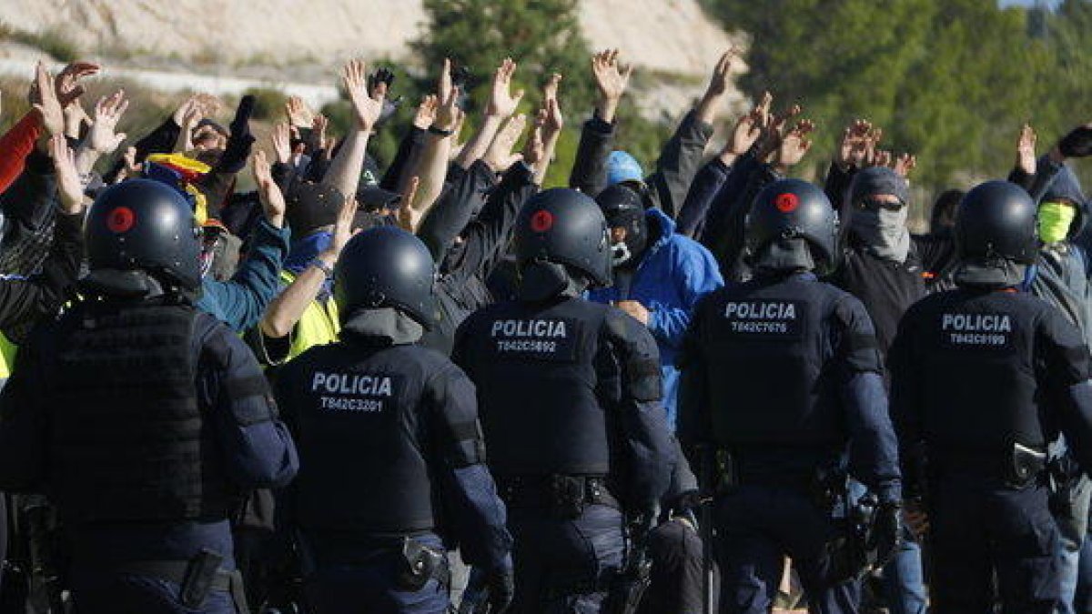 Participants del tall de l'AP-7 a Vandellòs aixequen les mans mentre agents dels antidisturbis dels Mossos d'Esquadra passen per davant d'ells.