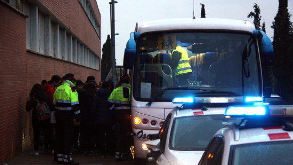 Un grupo de escolar bajando del autocar a las puertas de l'IES Roquetes mientras los Mossos D'Esquadra inician el control de los vehículos.