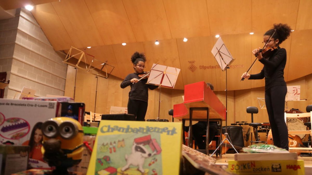 Dos violinistas en el escenario del conservatorio e imágenes de algunos juguetes