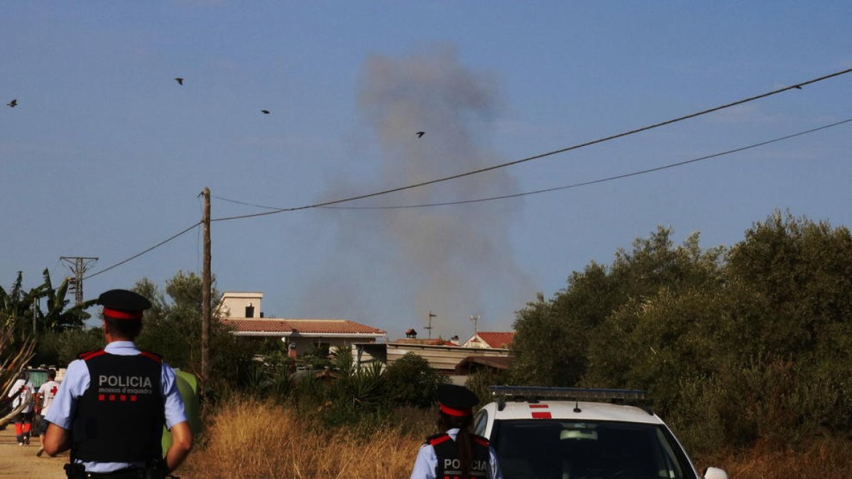 Dos agents dels Mossos d'Esquadra d'esquena, amb una columna de fum al davant durant una detonació controlada a Alcanar.