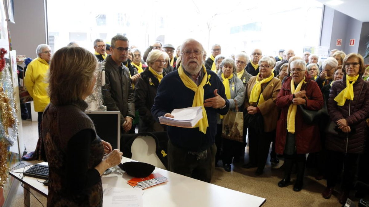 Plano medio del portavoz de los 'Avis i àvies per la llibertat' de Reus entregando las cartas de queja en la oficina del Síndic, desplazada a la capital del Baix Camp, con miembros del colectivo al fondo.