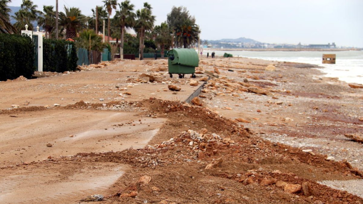 Carretera d'accés a la Platjola de les Cases d'Alcanar plena de sorra i roques mentre els operaris ho netegen.