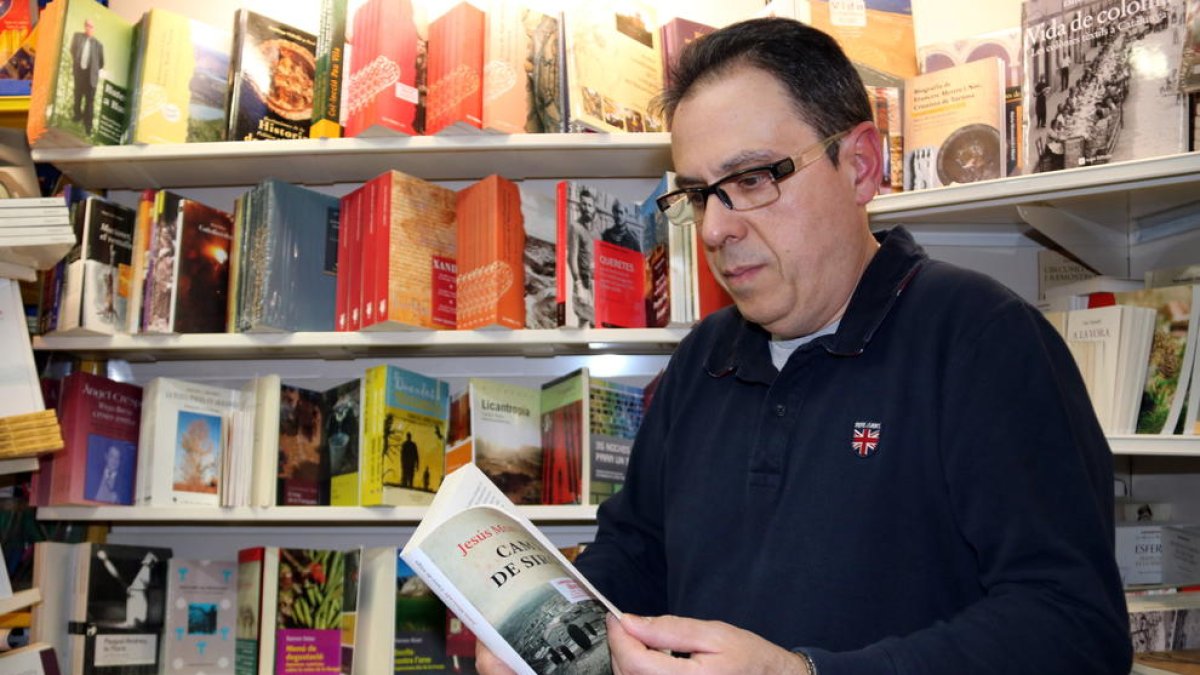 Plano medio de Octavi Serret, en medio de los libros de su establecimiento de Valderrobres, hojeando un ejemplar del 'Camino de Sirga' de Jesús Moncada.