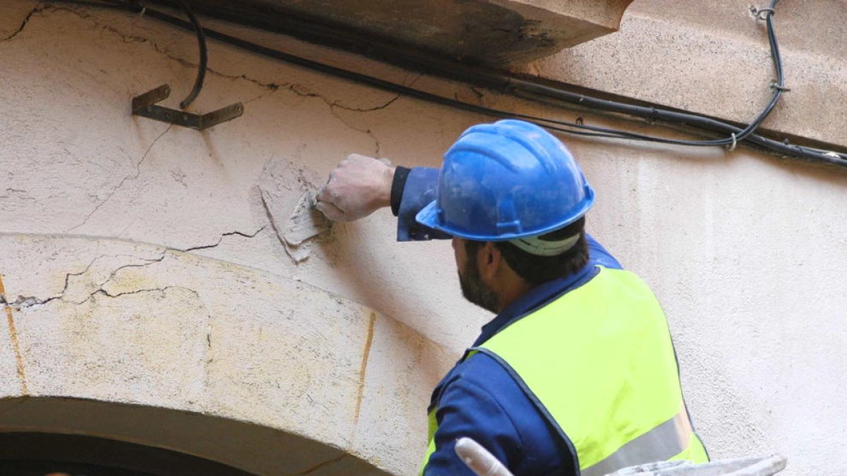 Un operari posa testimonis de guix damunt les esquerdes aparegudes en la façada d'un edifici.