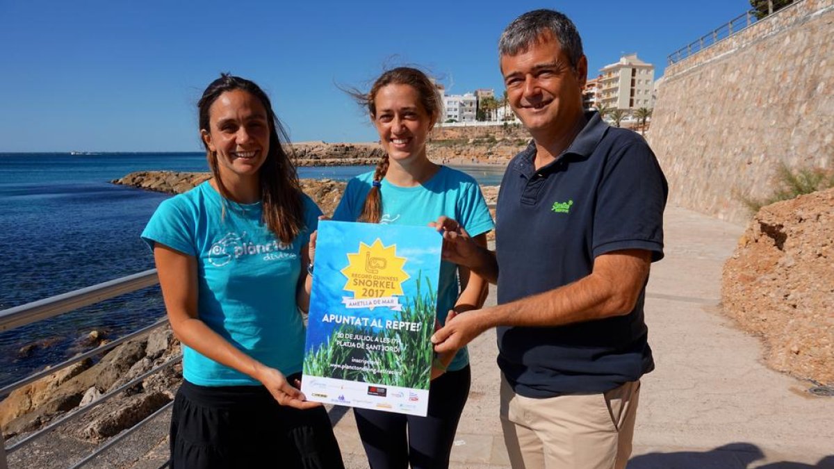 Les copropietàries de l'empresa organitzadora, Plàncton Diving, i l'alcalde de l'Ametlla de Mar, amb el cartell de l'esdeveniment.