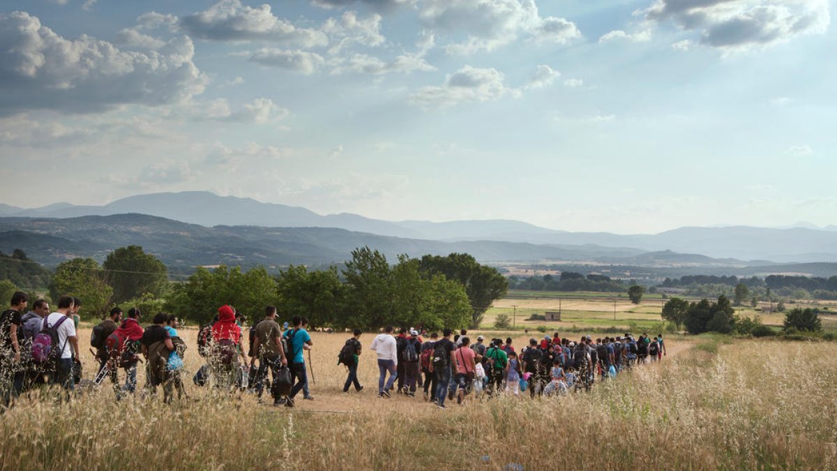 Un grup de centenars de refugiats amb hones, dones i nens camina camp a través a Europa, en un pla general.