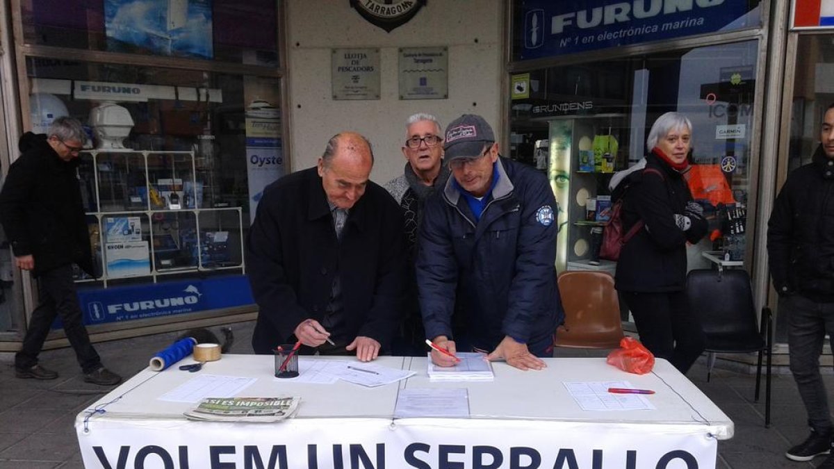 Dos veïns signen el document, a la mesa situada al raser de la Llotja del Serrallo.