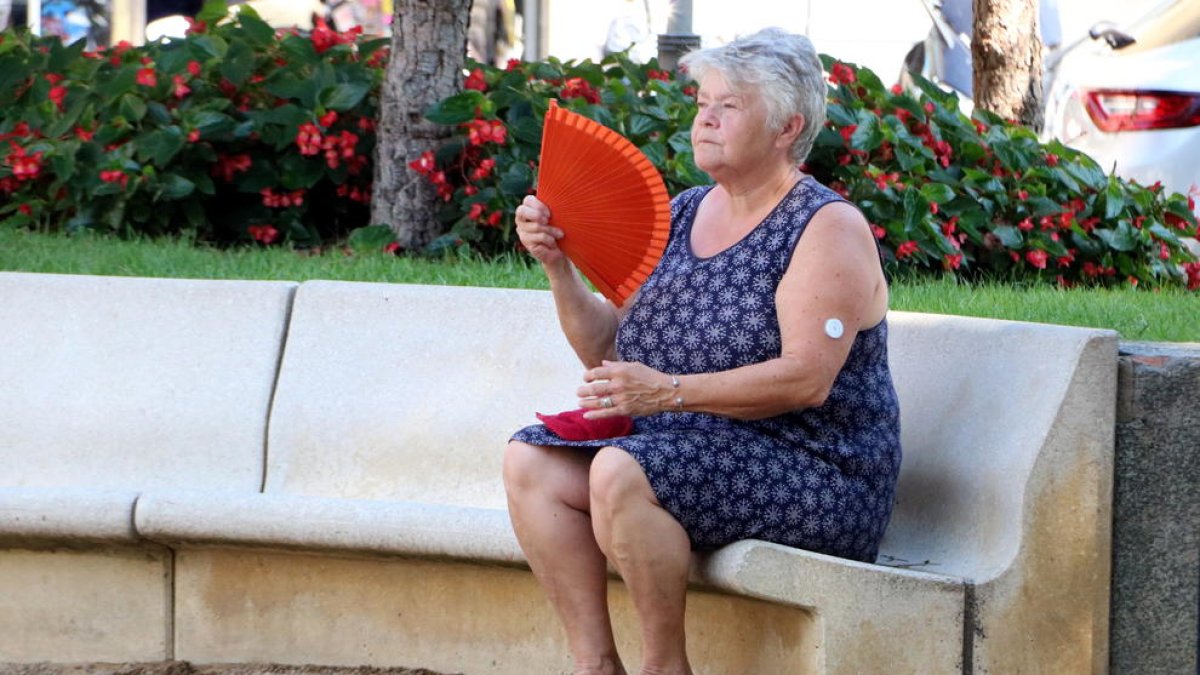 Una dona fent-se vent amb un ventall en una plaça pública de Figueres davant l'onada de calor.