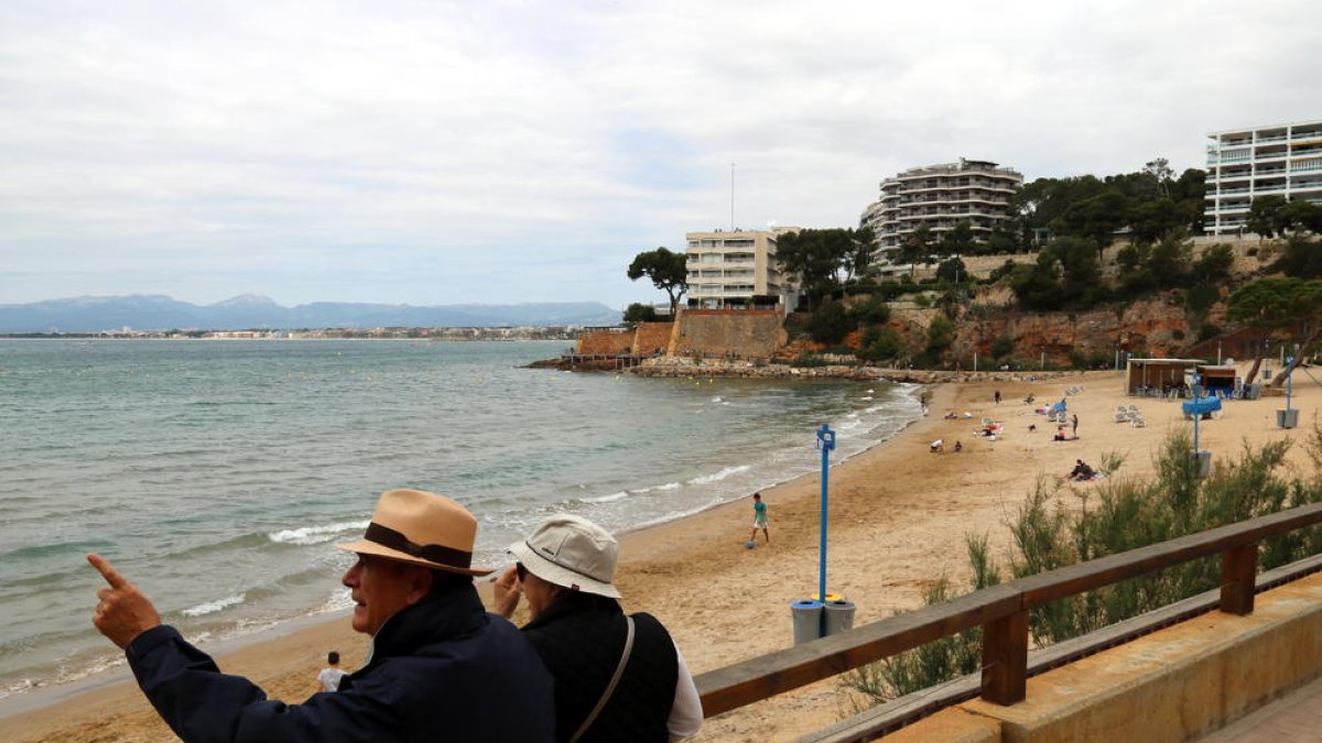 Pla general de la platja dels Capellans de Salou, amb uns turistes en primer terme. Imatge del 10 de maig del 2018