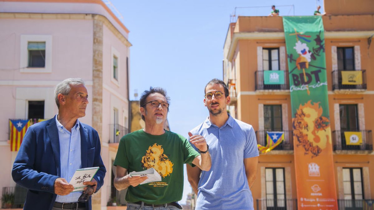 Josep Bertran, Enric Garriga y el diseñador Edu Polo en el Pla de la Seu, con la lona conmemorativa colgada detrás.