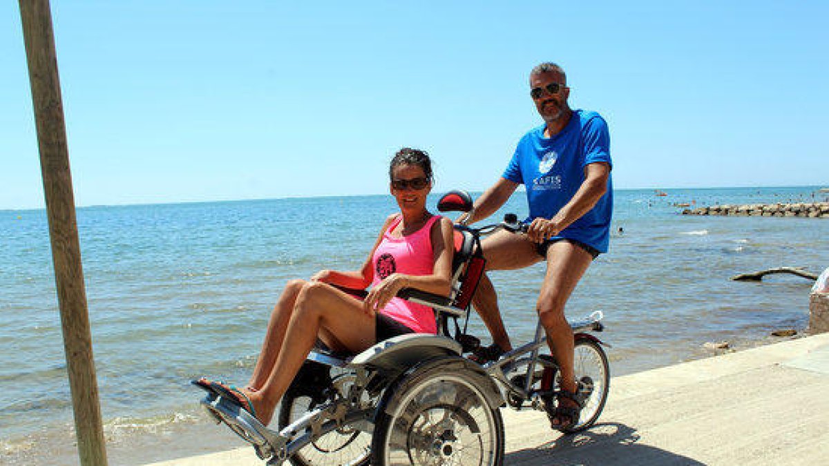 Una parella passeja prop de la platja amb una cadira-bicicleta adaptada OPair.