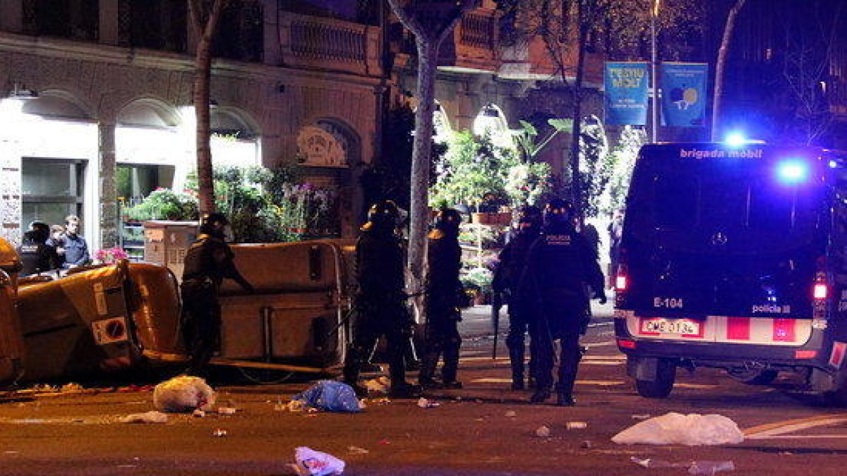 Plano general de agentes antidisturbios de los Mossos D'Esquadra retirando contenedores tumbados en medio de la calle a Barcelona durante los disturbios posteriores a la manifestación del 25 de marzo