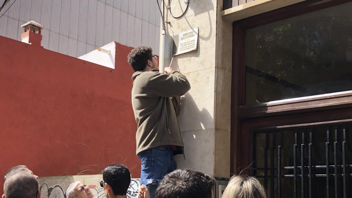 Pla obert d'un home retirant una placa franquista d'un immoble de Reus l'1 de maig del 2019
