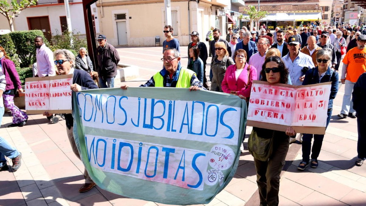 Plano general de manifestantes llevando carteles reivindicativos sobre las pensiones en la salida de la marcha por el centro de Amposta.