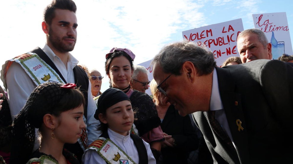 El president de la Generalitat, Quim Torra, rebut per dues nenes en la seva arribada al Centre Fluvial del Delta i amb pancartes al fons de protesta.