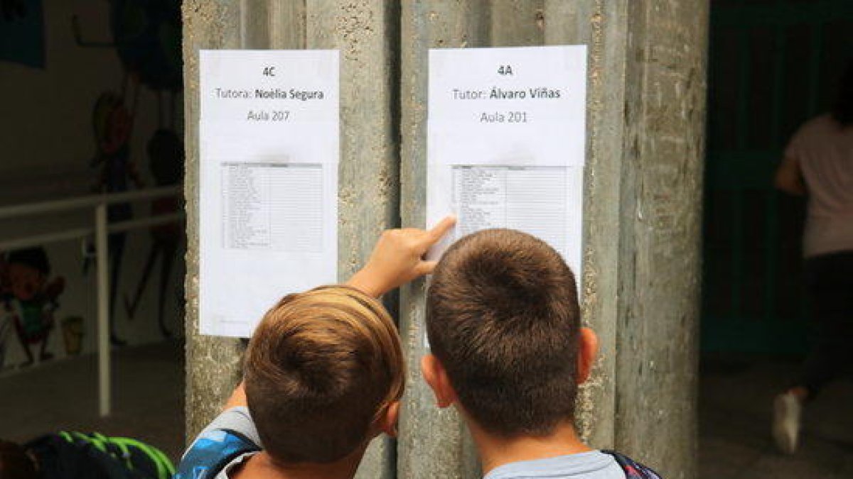 Dos nens observant la llista d'alumnes per aula a l'entrada de l'escola de Ferreries.