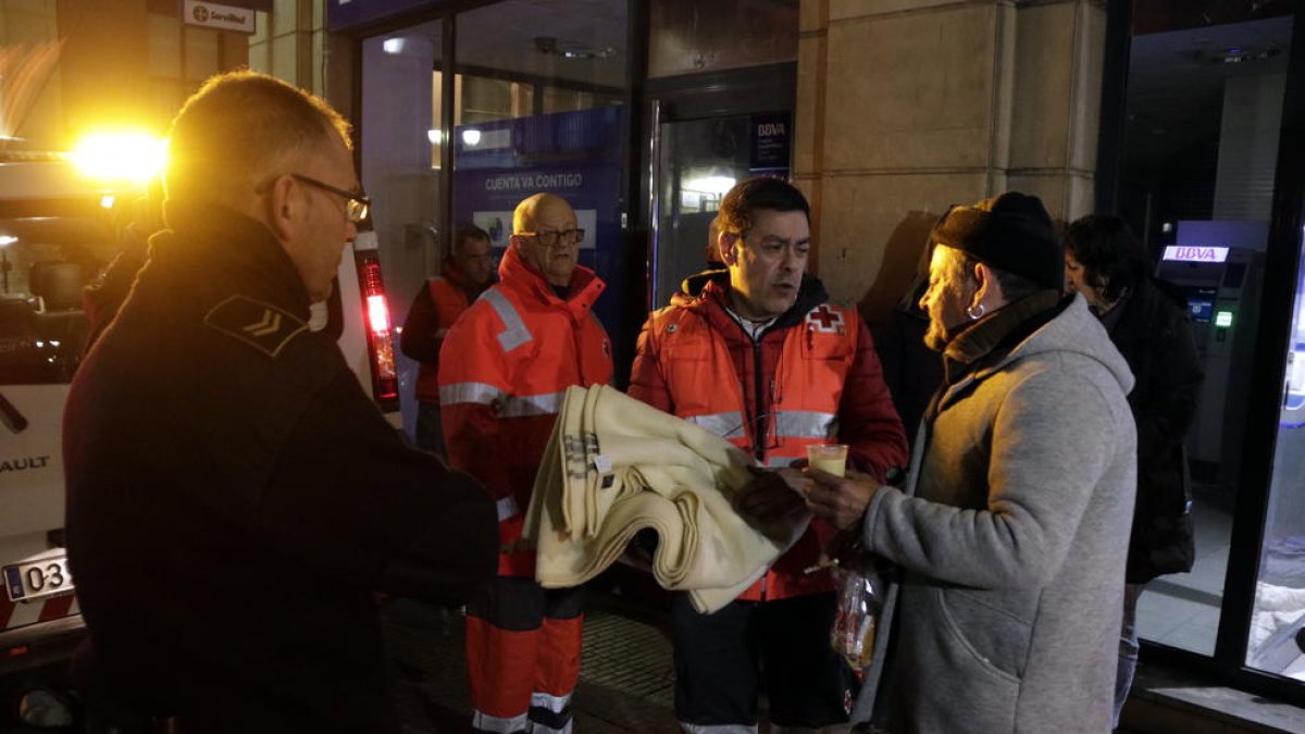 Pla americà de voluntaris de la Creu Roja lliurant una manta i un got de caldo a en Francisco Moreno, un sensesostre que passa la nit en un caixer de Tarragona. Imatge de l'11 de gener del 2018