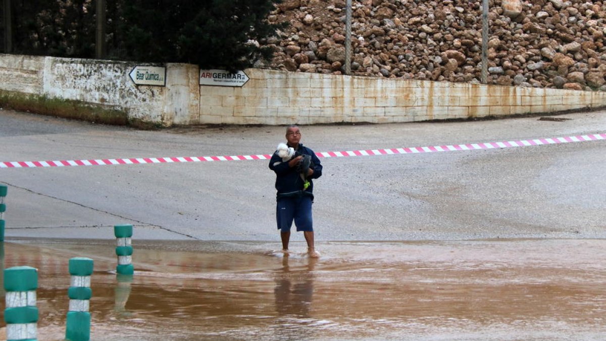 Un hombre hombre atravesando el barranco de la Galera, en Masdenverge, con el perro en los brazos.