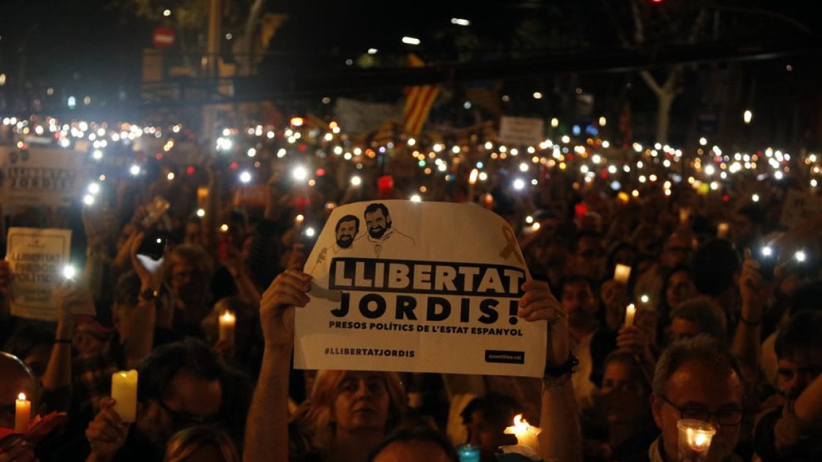 Un hombre sostiene una pancarta de 'Libertad Jordis' y, a su alrededor, personas con velas encendidas.