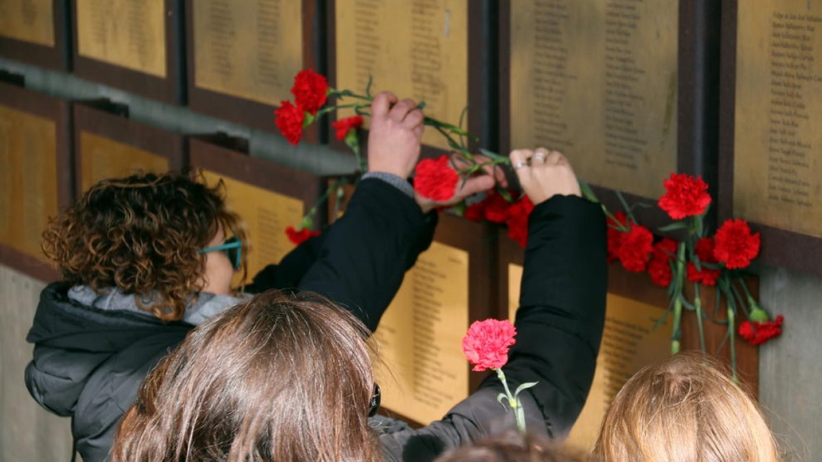Alguns familiars dipositant clavells rojos sota les plaques que recorden les víctimes de la Guerra Civil al memorial de les Camposines.