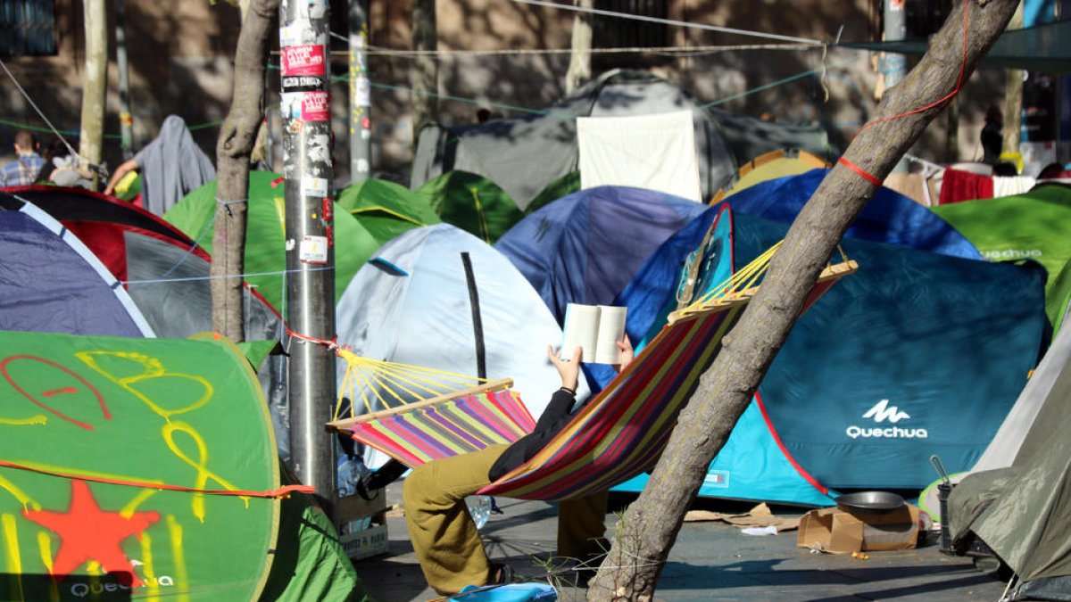 Una persona descansa llegint a l'acampada de Plaça Universitat.