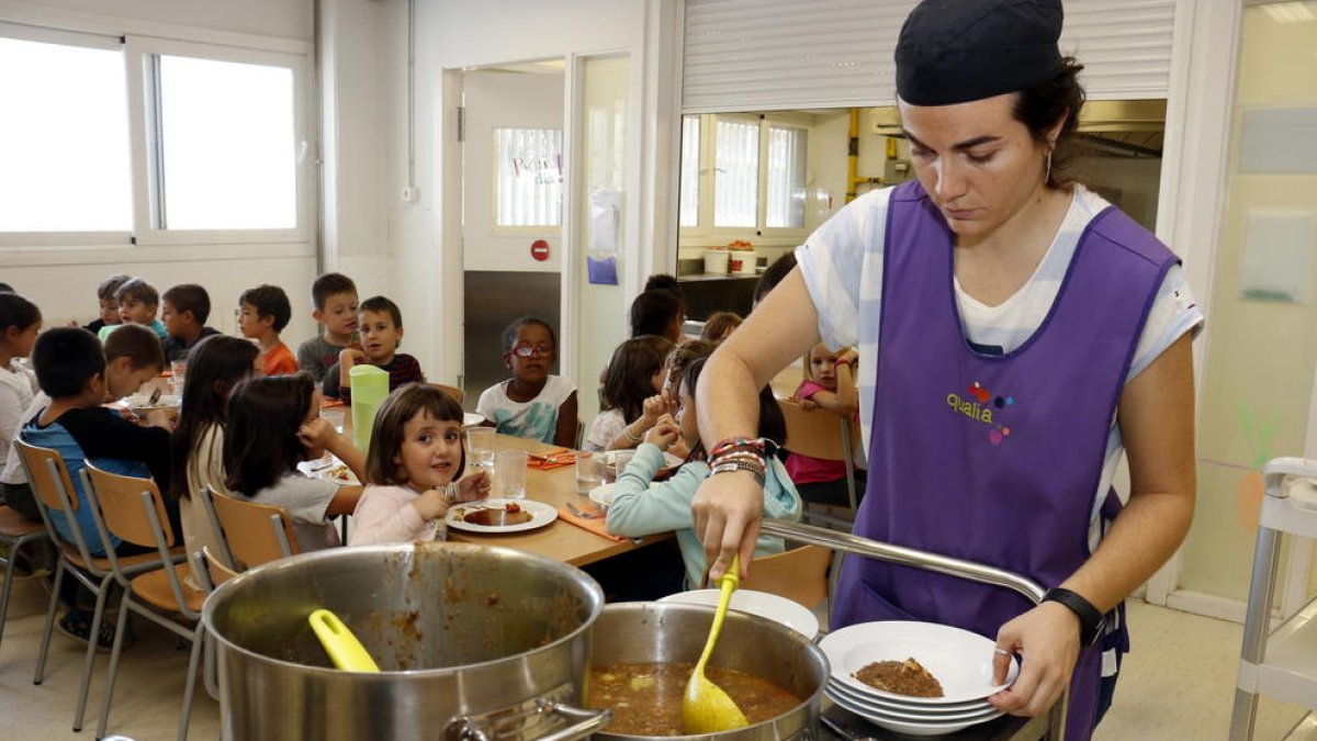 Una monitora sirviendo comida al plato en el comedor escolar.