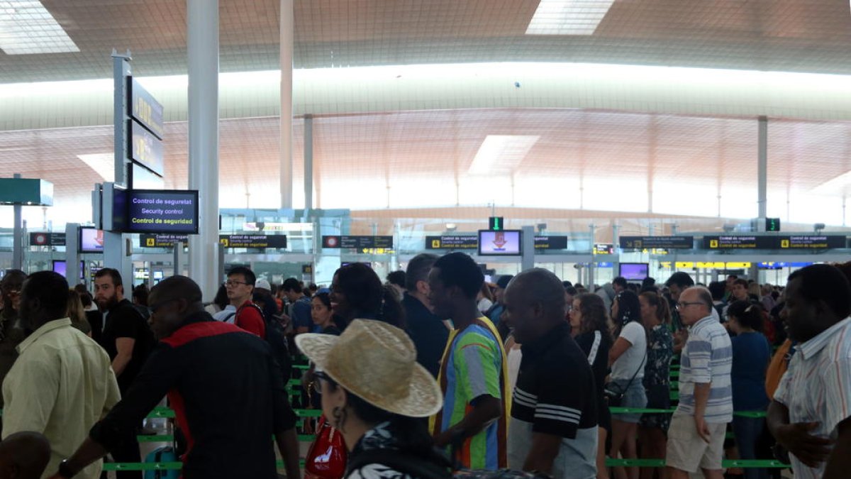 Diverses persones fent cua al control de seguretat de sortida de la T-1 de l'aeroport de Barcelona.