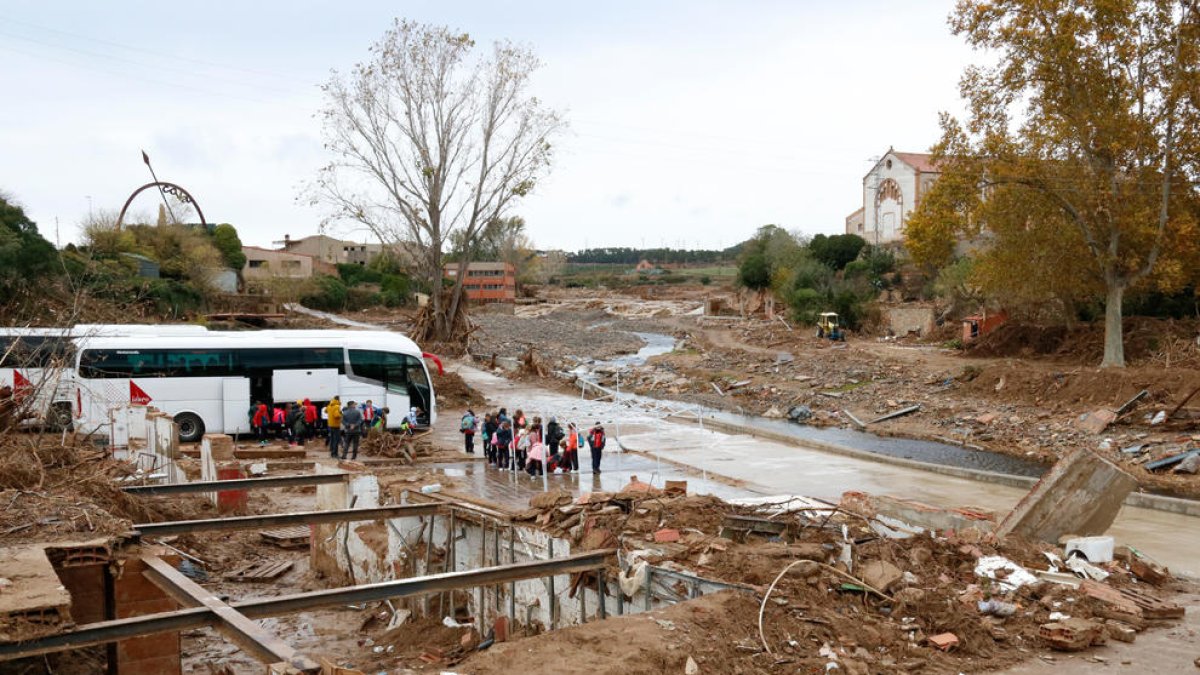 Pla general del riu Francolí al seu pas per l'Espluga de Francolí, de les destrosses a la llera i, al fons, un grup d'escolars de Barcelona baixant d'un autobús, de visita al poble. Imatge del 14 de novembre del 2019