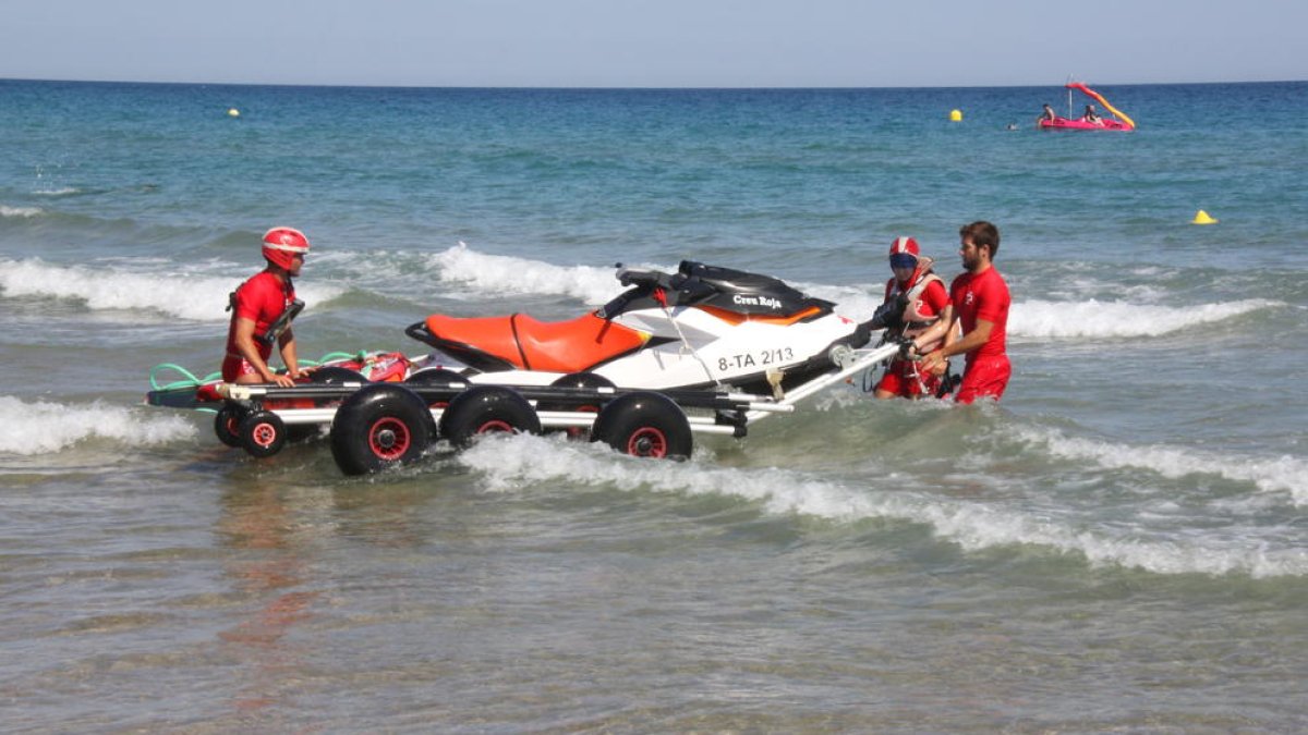 Los socorristas de la Cruz Roja entrando la moto acuática al agua, en la playa de l'Arrabassada de Tarragona.