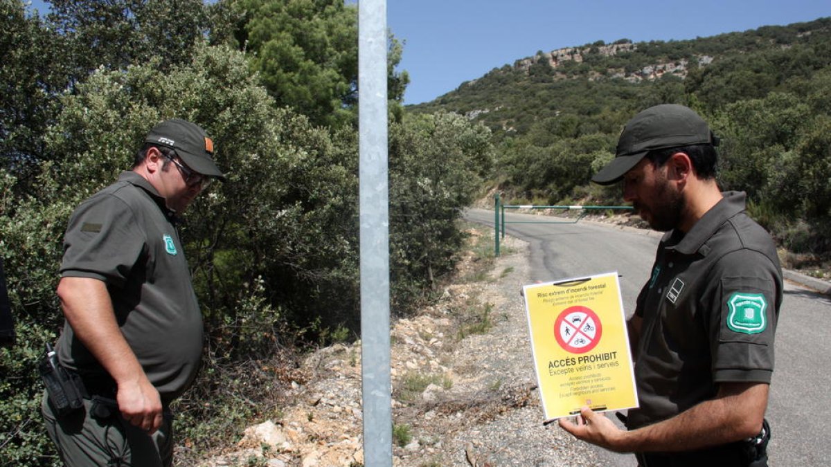 Dos efectivos de los Agents Rurals a punto de colocar un cartel que indica que está prohibido acceder a la sierra del Montsec.