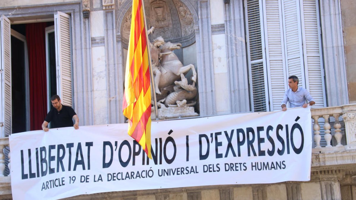 Membres de l'equip del president del Govern, Quim Torra, col·loquen la nova pancarta a la façana de Palau.