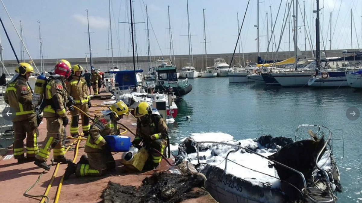 Bombers actuant al port de Torredembarra davant l'embarcació que ha cremat.