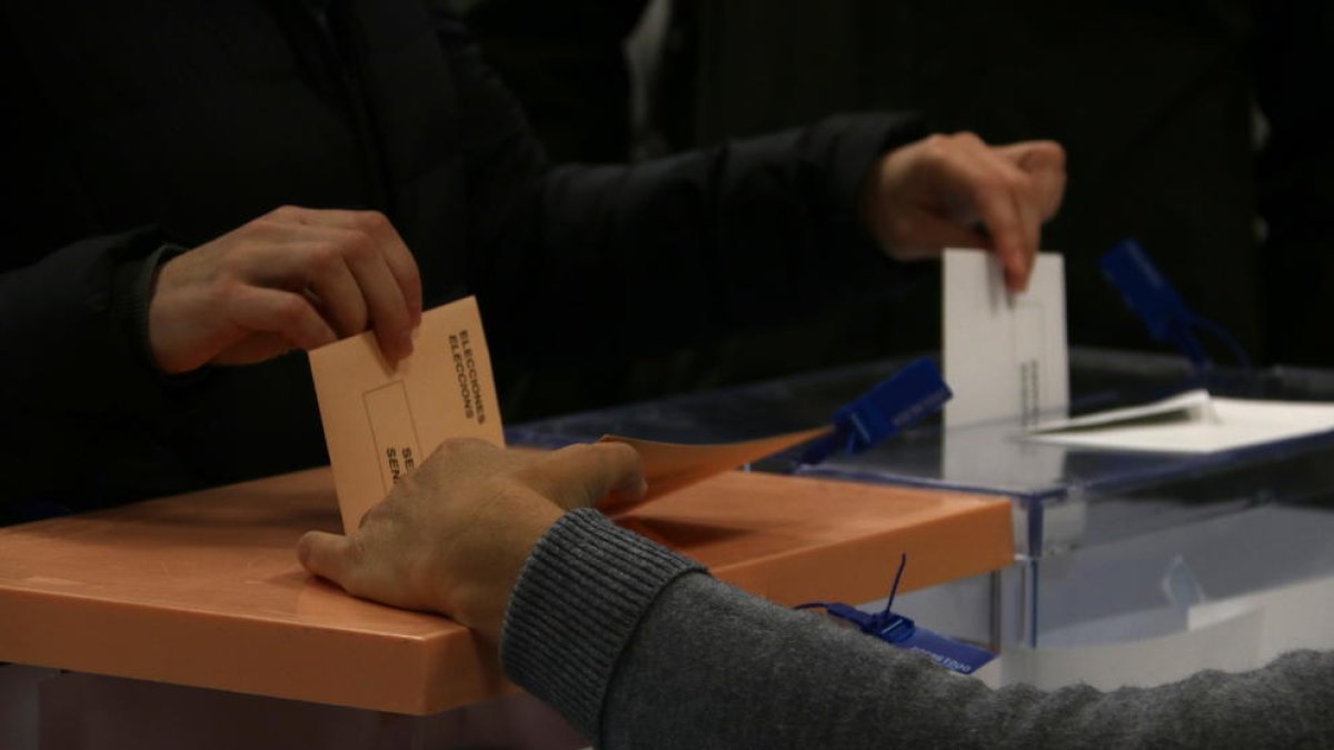 Plano detalle de una mano depositando las papeletas de las elecciones en el Congreso de los diputados y al Senado en una urna.