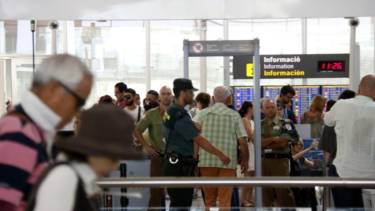 Passatgers passant el control de seguretat davant un agent de la Guàrdia Civil i dos vigilants a la T1 de l'aeroport del Prat.
