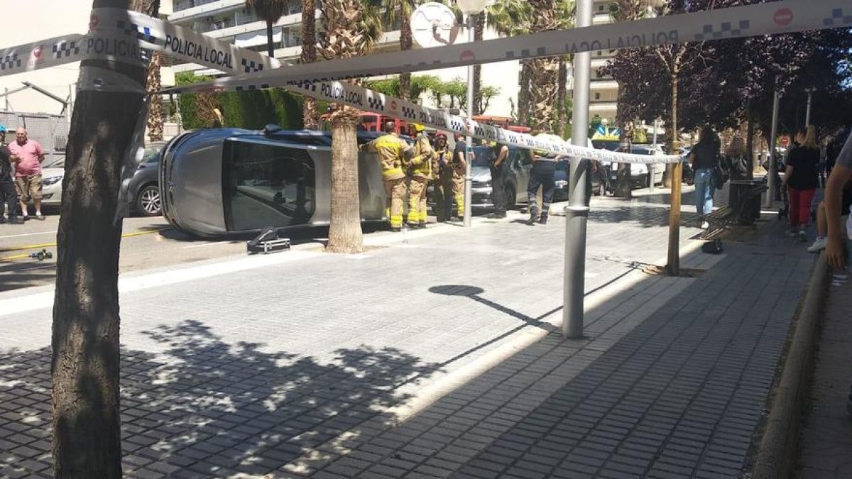 Imatge de la zona acordonada per la Policia Local amb el cotxe bolcat de fons i efectius dels Bombers treballant en el servei.