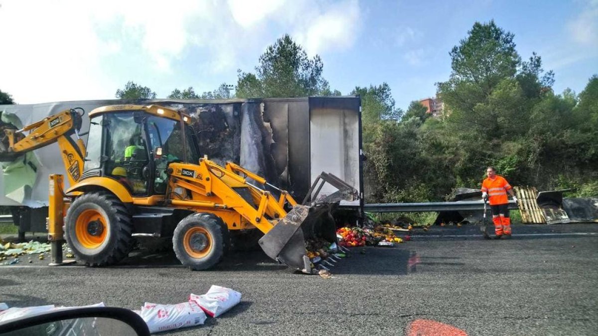 Imagen del camión incendiado, con las frutas y verduras en el suelo y operarios trabajando en la retirada de la mercancía.