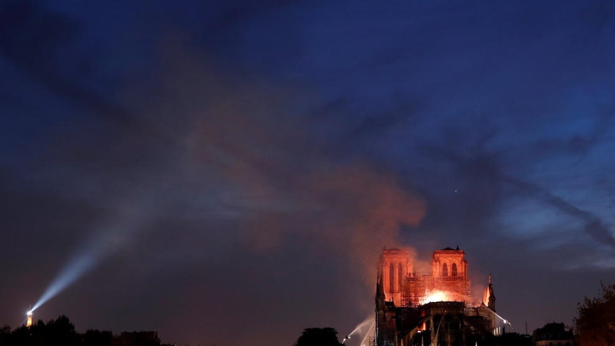 La Catedral de Notre-Dame de París en flames durant la nit, amb bombers remullant l'edifici per intentar salvar les torres.